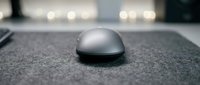 Computer mouse on gray desk surface with blurred office background, suitable for technology and workspace design projects.