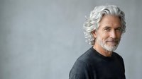 Mature man with white hair and beard wearing dark sweater against neutral gray background, suitable for senior lifestyle, healthcare, and corporate portraits.