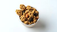 Homemade granola with nuts and dried fruits in white bowl on clean background for healthy breakfast and snacking concepts.