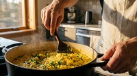 Senior man stirring paella with wooden spoon in kitchen, preparing traditional Spanish rice dish with vegetables and seafood for cooking and culinary content.