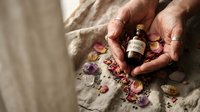 Hands holding essential oil bottle with dried flower petals on linen fabric for natural aromatherapy wellness spa treatment and holistic healing.