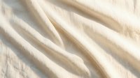 Soft cream colored fabric with elegant flowing folds and gentle waves creating luxurious textile background for fashion and interior design projects.