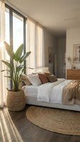 Serene bedroom interior with natural sunlight streaming through large windows, featuring a white bed with neutral pillows, potted green plant in woven basket, and round jute rug.
