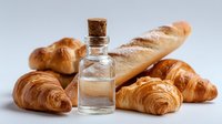 Artisanal bakery assortment with glass bottle of salt or yeast on white background, featuring croissants, baguette and bread rolls for food photography.