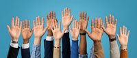Diverse group of business professionals raising hands in voting gesture against blue background showing teamwork and democratic participation.