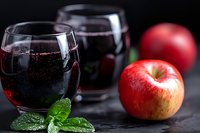 Refreshing red apple juice in elegant glasses with fresh mint garnish on dark slate background, perfect for beverage menus.
