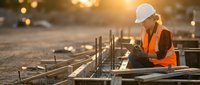 Construction worker in safety gear inspecting concrete foundation with rebar at sunset. Professional builder wearing hard hat and high-visibility vest on site.