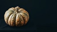 Aged pumpkin with weathered tan and brown striped skin isolated on dark background, suitable for autumn harvest designs and seasonal marketing materials.