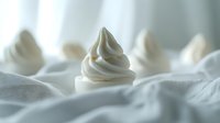 Soft swirls of white meringue or whipped cream peaks arranged on light fabric background creating dreamy minimal composition with selective focus and bokeh effect.