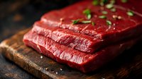 Fresh raw beef steak on rustic wooden cutting board garnished with herbs and salt, dark moody background with selective focus for food photography.