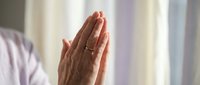 Senior woman hands in prayer position wearing wedding ring showing faith and spirituality in soft natural light for meditation and religious concepts.