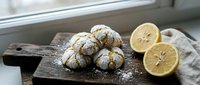 Homemade lemon crinkle cookies dusted with powdered sugar on rustic wooden cutting board with fresh lemon slices for baking and dessert recipes.