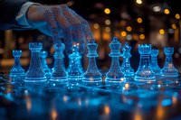Glowing blue glass chess pieces on reflective board with player's hand making move, illuminated by ambient bokeh lights creating magical atmosphere.