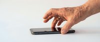 Mature man with age spots and wrinkles using smartphone on white surface. Senior male hand touching mobile device screen for communication, technology adoption, or digital learning purposes.