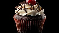 Chocolate cupcake topped with vanilla buttercream frosting, chocolate drizzle, chocolate shavings and maraschino cherry against dark background. Food photography.