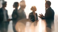 Business professionals engaged in conversation at corporate networking event, silhouetted against bright background creating atmospheric mood.