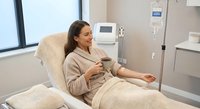 Young Caucasian woman patient relaxing in modern medical chair during IV therapy treatment in bright healthcare facility with professional equipment.