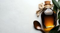 Amber glass bottle with cork stopper filled with golden oil, wooden spoon, and green leaves on white textured surface for wellness and beauty product packaging design.