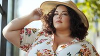 Plus-size Hispanic woman in floral dress and wide-brimmed hat posing confidently outdoors. Summer fashion portrait for body positivity campaigns and lifestyle content.