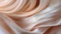 Soft flowing waves of peach and cream colored silk fabric create elegant abstract curves and folds with gentle light and shadow play. Luxurious textile background.