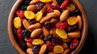 Mixed nuts and dried fruits in wooden bowl on dark slate background for healthy snacking and cooking ingredients.