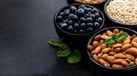 Fresh blueberries, almonds and quinoa in black ceramic bowls on dark background with mint leaves, healthy superfood ingredients for cooking and snacks.