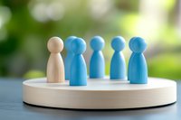 Wooden figures on white platform showing diversity concept - one beige figure standing with blue figures representing teamwork and inclusion in business.