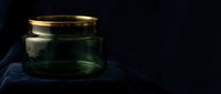 Empty glass jar with gold lid on dark blue fabric against black background, suitable for product mockups and packaging design.