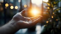 Open palm reaching towards bright sunlight creating magical glow effect with bokeh lights and natural lens flare in background, spiritual healing concept.