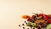 Aromatic spices collection with cinnamon sticks, star anise, dried chili peppers, cardamom pods and peppercorns on neutral background for culinary use.
