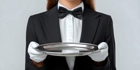 Female server in formal black tuxedo and bow tie holding empty silver serving tray with white gloves against gray background.