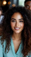 Young mixed-race woman with curly hair smiling warmly in casual turquoise shirt with soft bokeh lighting background for lifestyle and portrait photography.