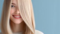 Young Caucasian woman with straight blonde hair and bright smile wearing light sweater against blue background, beauty and fashion portrait with natural makeup look.