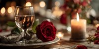 Elegant romantic dinner table setting with wine glass, red rose, candle and warm bokeh lights for Valentine's Day celebration or anniversary date.