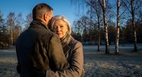 Happy mature couple embracing in winter park during golden hour sunset. Romantic senior man and woman sharing intimate moment outdoors in snowy landscape.