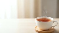 Steaming hot tea cup on wooden saucer placed on white table with soft natural lighting and blurred curtains creating cozy morning atmosphere.