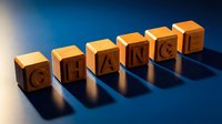 Wooden letter blocks spelling CHANGE on blue surface with dramatic lighting creating shadows for business transformation and personal development concepts.