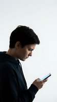 Young Caucasian man in dark shirt using smartphone, profile view on white background. Digital communication, social media, mobile technology concept.