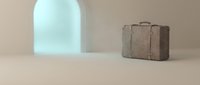 Minimalist composition with vintage leather suitcase and arched doorway casting soft shadows on neutral beige surface for travel and lifestyle concepts.