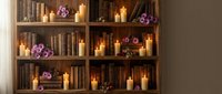 Cozy wooden bookshelf with vintage books, glowing candles and purple flowers creating warm atmospheric home library interior for relaxation and reading.
