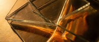 Elegant crystal whiskey glass with amber liquid on wooden surface creating warm reflections and sophisticated drinking atmosphere for luxury lifestyle.
