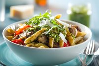 Gourmet pasta dish with roasted vegetables, mushrooms, and fresh arugula garnish in white bowl, served on turquoise placemat for food blog or restaurant menu.