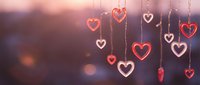 Romantic heart decorations hanging on strings with warm bokeh lights creating dreamy Valentine's Day atmosphere for love celebration backgrounds.