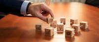 Businessman hand arranging wooden cubes with business icons on office desk representing strategic planning and organizational management concepts.