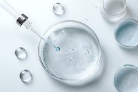 Cosmetic serum drop falling into glass petri dish with clear liquid, surrounded by water drops and laboratory glassware on white background. Professional skincare concept.