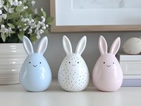 Decorative ceramic easter bunny figurines in pastel colors with cute smiling faces and long ears arranged on white surface with spring flowers in background.