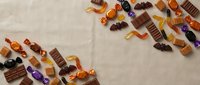 Assorted colorful candies and chocolates scattered on neutral linen fabric background creating sweet confectionery flat lay composition for food photography.