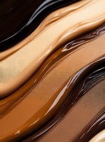Smooth flowing layers of foundation makeup in various skin tones from light to dark, creating a wavy pattern for cosmetic advertising.