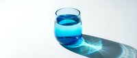 Clear glass filled with bright turquoise liquid casting a shadow with light refraction on white surface, suitable for beverage, wellness and hydration concepts.