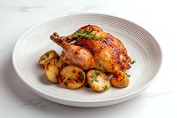 Roasted golden-brown chicken with crispy skin served on white ceramic plate with herb-seasoned baby potatoes, garnished with fresh herbs on marble surface.